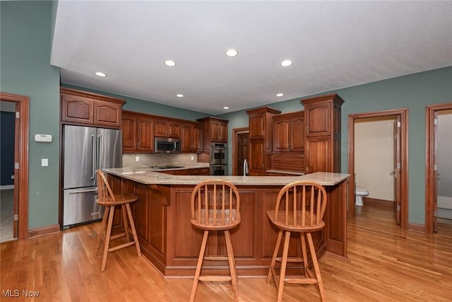 kitchen featuring stainless steel appliances, a kitchen breakfast bar, backsplash, a spacious island, and light wood-type flooring