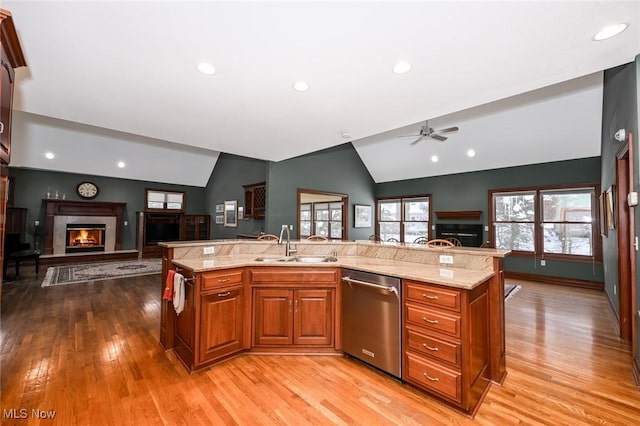 kitchen featuring stainless steel dishwasher, sink, a kitchen island with sink, and vaulted ceiling