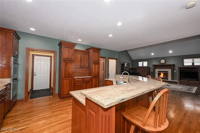 kitchen featuring double wall oven, sink, a center island with sink, hardwood / wood-style floors, and a breakfast bar area