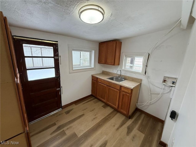 clothes washing area with hookup for a washing machine, cabinet space, a sink, a textured ceiling, and light wood-type flooring