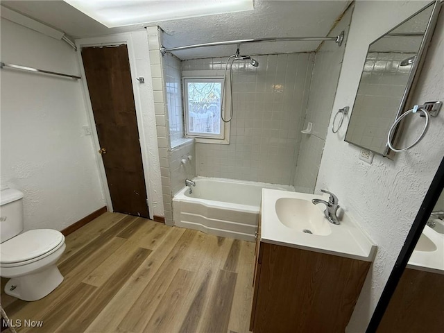 full bathroom featuring toilet, shower / washtub combination, wood finished floors, vanity, and a textured wall