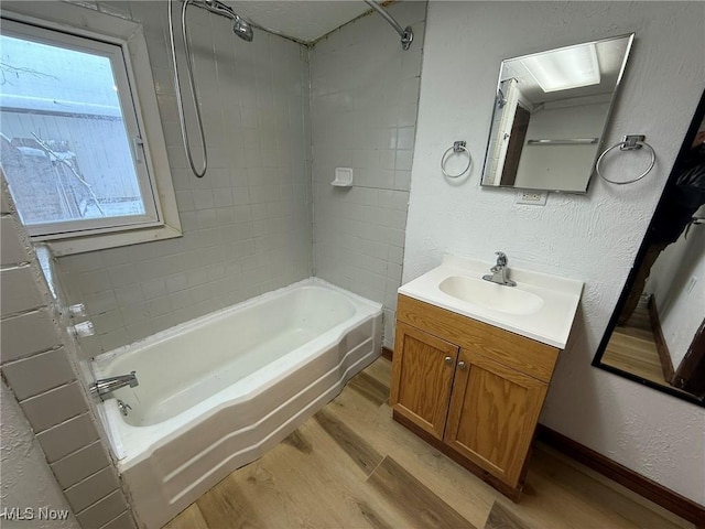 bathroom featuring vanity, wood finished floors, baseboards, shower / bathing tub combination, and a textured wall