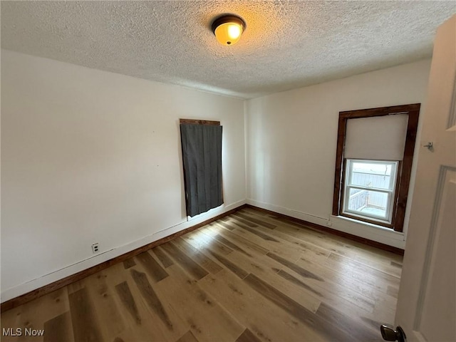 empty room featuring a textured ceiling, baseboards, and wood finished floors