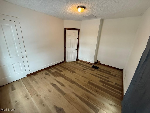 unfurnished room with light wood-type flooring, baseboards, and a textured ceiling