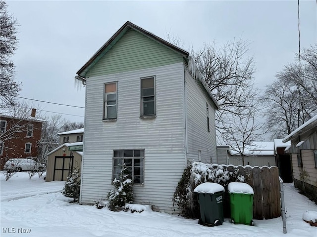 snow covered back of property featuring a storage shed, an outdoor structure, and fence