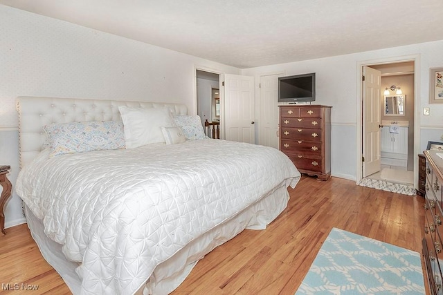 bedroom featuring connected bathroom and light hardwood / wood-style floors