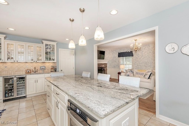 kitchen featuring white cabinetry, a center island, hanging light fixtures, beverage cooler, and a fireplace