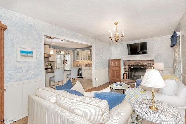 living room with a brick fireplace, a chandelier, beverage cooler, and light hardwood / wood-style flooring