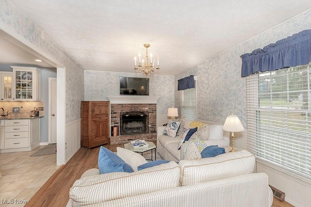 living room with a brick fireplace, light hardwood / wood-style flooring, a notable chandelier, and sink