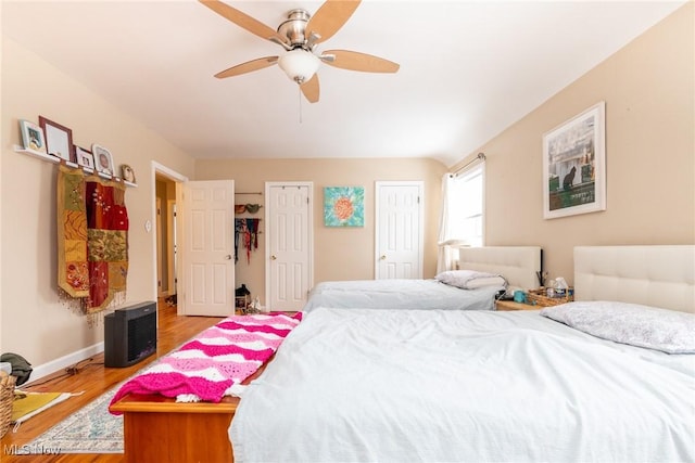 bedroom with hardwood / wood-style floors, two closets, and ceiling fan