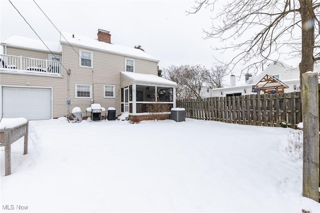 snow covered rear of property featuring a sunroom