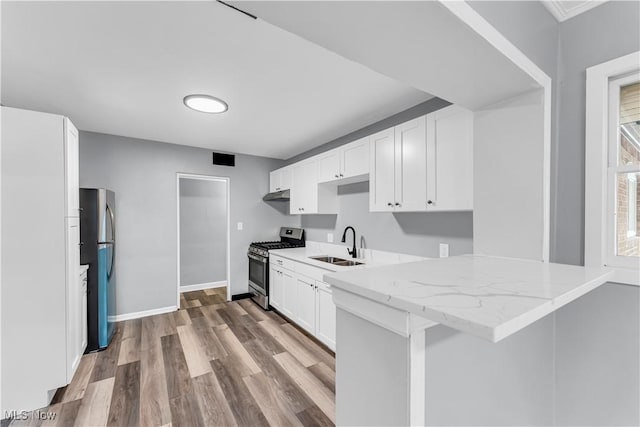 kitchen featuring sink, stainless steel appliances, light stone counters, kitchen peninsula, and white cabinets