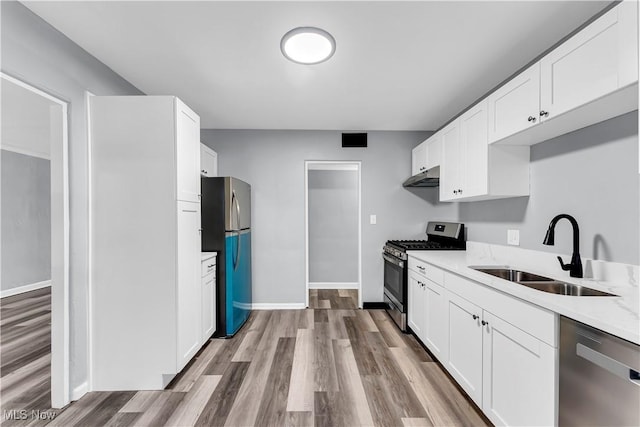 kitchen featuring appliances with stainless steel finishes, light wood-type flooring, light stone counters, sink, and white cabinetry