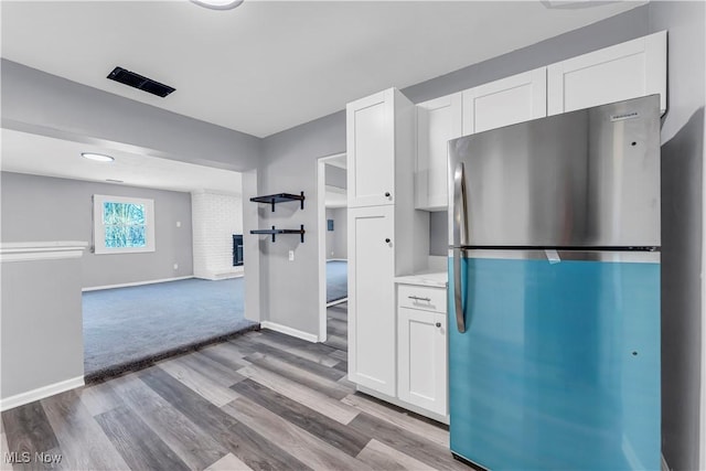 kitchen with stainless steel fridge, light wood-type flooring, and white cabinetry