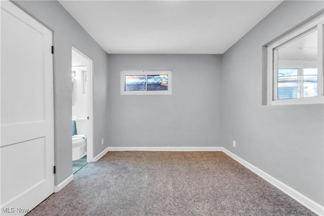 unfurnished bedroom featuring carpet, ensuite bath, and multiple windows