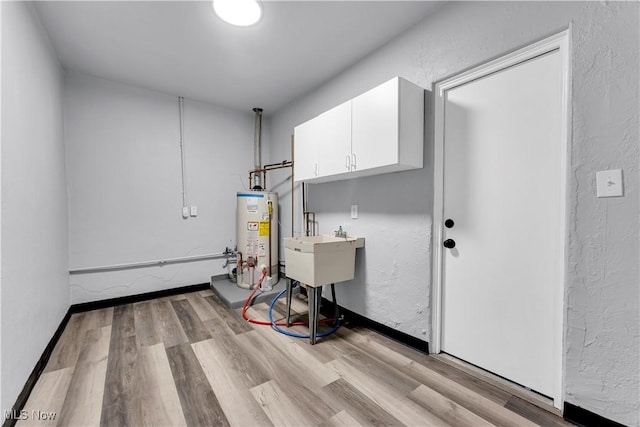 laundry area featuring cabinets, baseboard heating, sink, water heater, and light hardwood / wood-style flooring