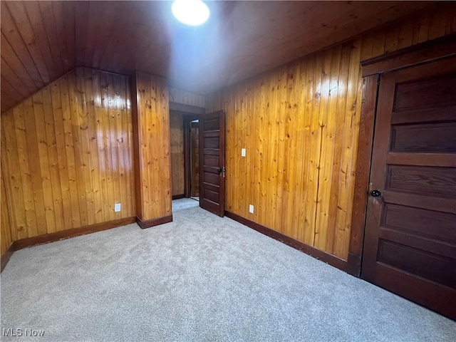 additional living space featuring light carpet, vaulted ceiling, and wooden walls