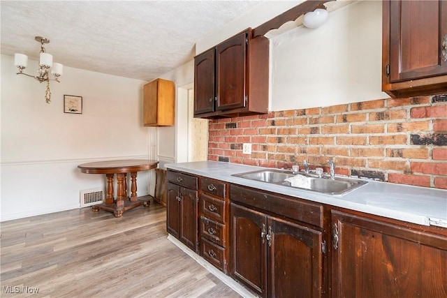 kitchen with sink, light hardwood / wood-style floors, decorative light fixtures, a textured ceiling, and dark brown cabinets