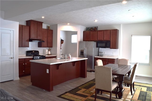 kitchen featuring a kitchen island with sink, black appliances, sink, light hardwood / wood-style floors, and a breakfast bar area