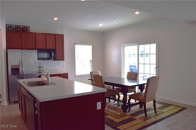 kitchen featuring sink, stainless steel fridge with ice dispenser, an island with sink, light hardwood / wood-style floors, and a textured ceiling