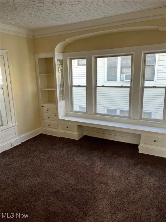 spare room with a textured ceiling, dark carpet, and ornamental molding