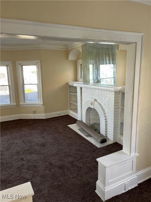 unfurnished living room featuring a fireplace, dark carpet, and ornamental molding