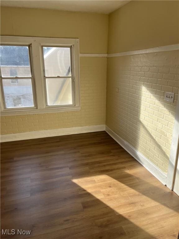 empty room with brick wall and hardwood / wood-style flooring