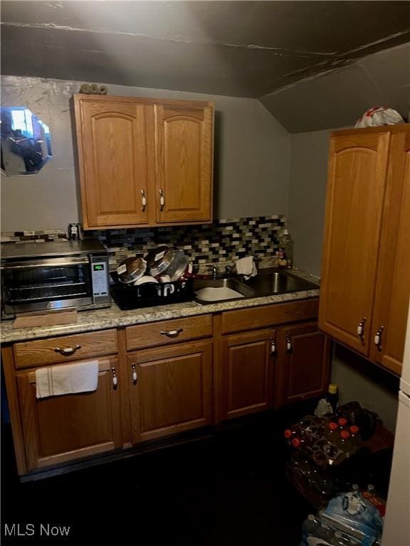 kitchen with tasteful backsplash, light stone counters, sink, and vaulted ceiling