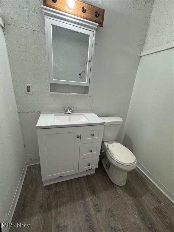 half bath with baseboards, vanity, toilet, and wood finished floors