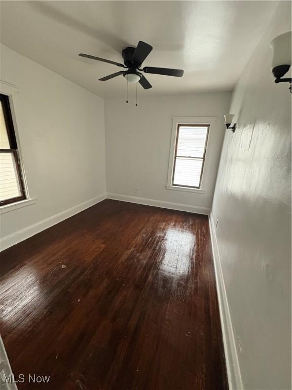 empty room with a ceiling fan, dark wood finished floors, and baseboards