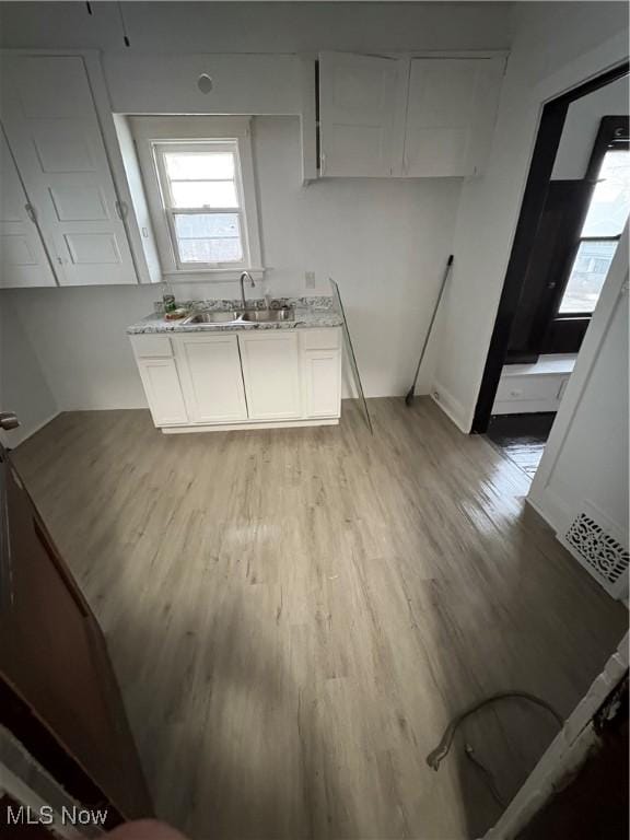 kitchen with light wood-style flooring, light stone counters, white cabinets, and a sink