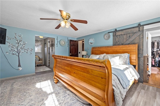 bedroom featuring hardwood / wood-style flooring, ceiling fan, a barn door, and a textured ceiling