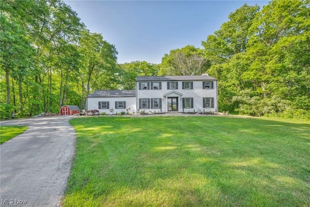colonial home with an outdoor structure, a front yard, driveway, and a storage unit