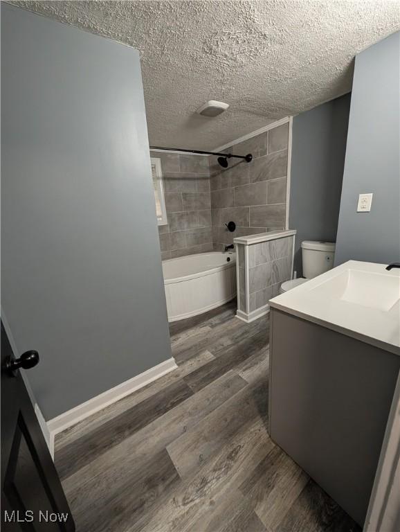 full bathroom featuring toilet, tiled shower / bath combo, a textured ceiling, and hardwood / wood-style flooring