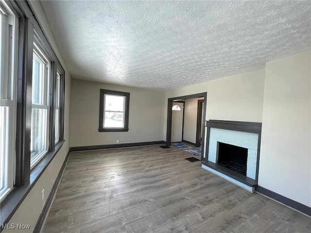 unfurnished living room featuring hardwood / wood-style floors, a textured ceiling, and a brick fireplace