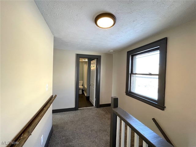 hall featuring dark carpet and a textured ceiling