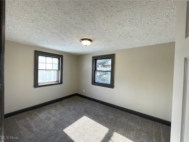 empty room featuring dark colored carpet, a textured ceiling, and plenty of natural light