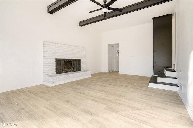 unfurnished living room featuring ceiling fan, beam ceiling, light wood-type flooring, and a brick fireplace