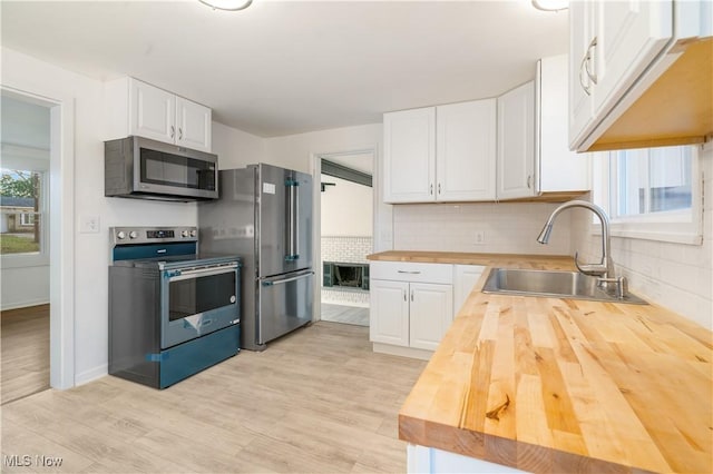 kitchen with butcher block counters, sink, light hardwood / wood-style flooring, white cabinets, and appliances with stainless steel finishes