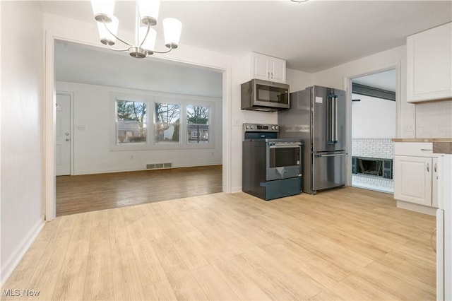 kitchen with white cabinetry, stainless steel appliances, a notable chandelier, pendant lighting, and light wood-type flooring