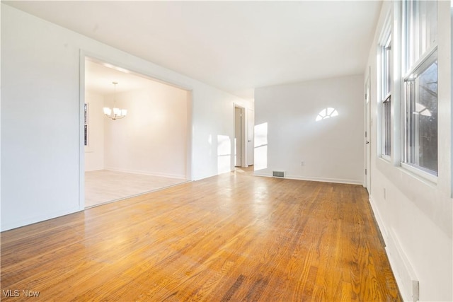 empty room with hardwood / wood-style flooring and an inviting chandelier