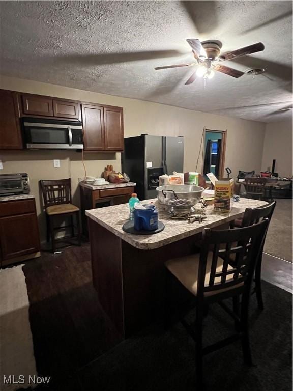 kitchen featuring a kitchen bar, dark brown cabinets, a textured ceiling, stainless steel appliances, and a kitchen island