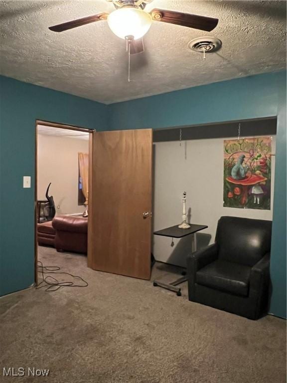 living area featuring a textured ceiling, carpet floors, and ceiling fan