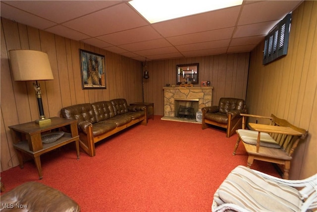 living room with a paneled ceiling, wooden walls, a fireplace, and carpet