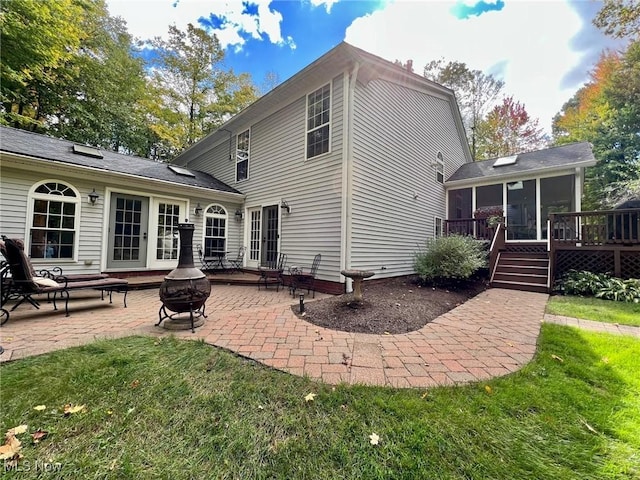 rear view of house featuring a sunroom, a lawn, a wooden deck, a patio, and an outdoor fire pit