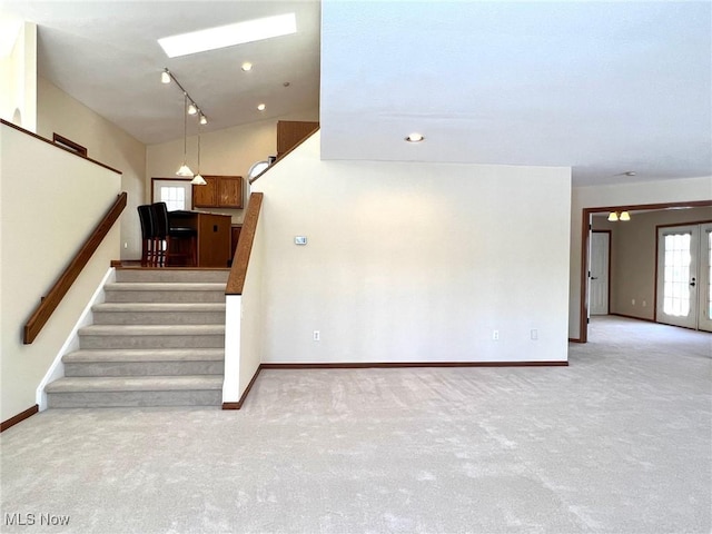 staircase featuring carpet floors, rail lighting, and lofted ceiling with skylight