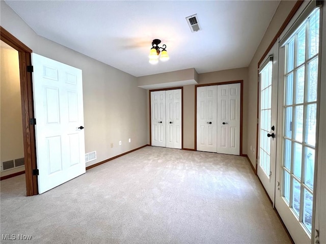 unfurnished bedroom with french doors, light carpet, and multiple closets