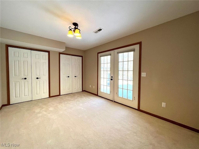 unfurnished bedroom featuring access to outside, french doors, light colored carpet, and two closets