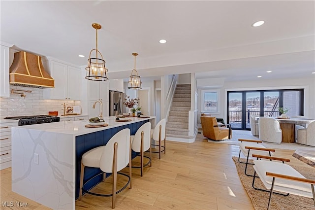 kitchen featuring white cabinetry, wall chimney range hood, stainless steel refrigerator with ice dispenser, an island with sink, and decorative backsplash