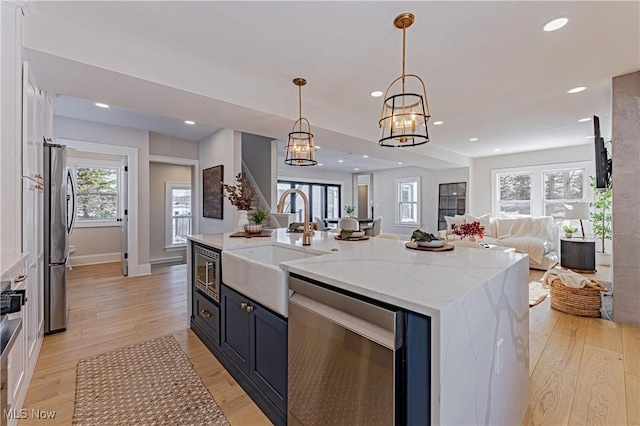 kitchen featuring light stone countertops, stainless steel appliances, sink, pendant lighting, and a center island with sink